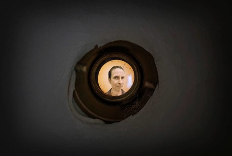 Woman seen out of focus through the old dirty peephole of the front door of a dark apartment
