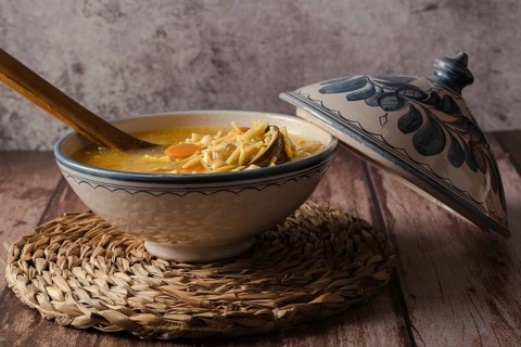 Tureen decorated with chicken soup with noodles on a wooden table