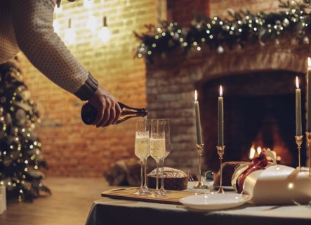 New Years Eve celebration. Man pouring champagne into glasses standing on table with festive xmas