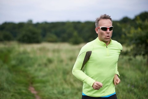Healthy fit man wearing sunglasses jogging through rural grassland on a country track with copy