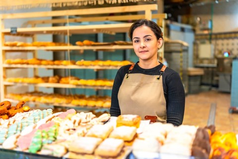Latin young saleswoman standing in the counter of a bakery shop with pastries and artisan bread