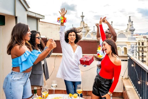 Happy man receiving a birthday gift celebrating with multi-ethnic friends during sunset rooftop