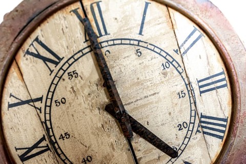 Old vintage and retro analogue clock displaying five o' clock. Worn-out and grunge style with