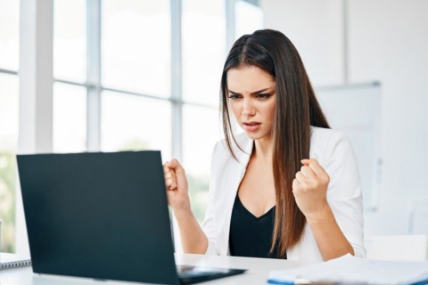 Shocked businesswoman looking at laptop reading bad news at her desk in modern office. Stressed and