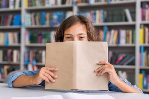 Boy covering his face with book library