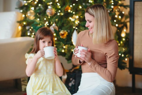 Happy family, mother and little daughter drinking hot cacao, sitting near decorated ?hristmas tree,