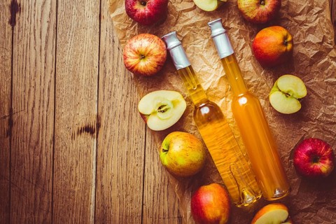 Apple juice with apple vinegar in bottles and fresh apples on wooden background