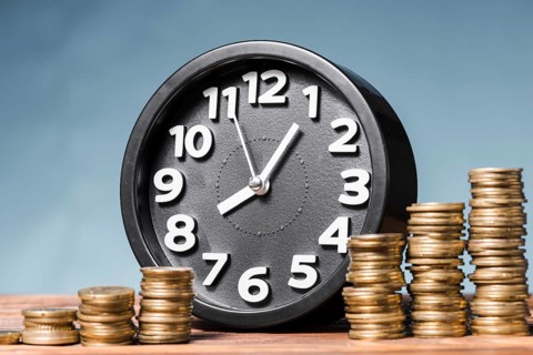 Round alarm clock with stack increasing coins against blue background. High resolution photo