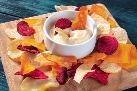 Vegetable chips with a dip on a wooden board, a healthy vegan snack
