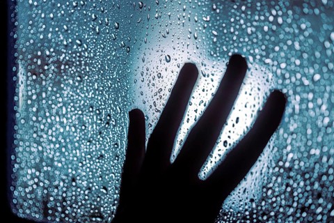 Close up of hand silhouette on window with water drops, night