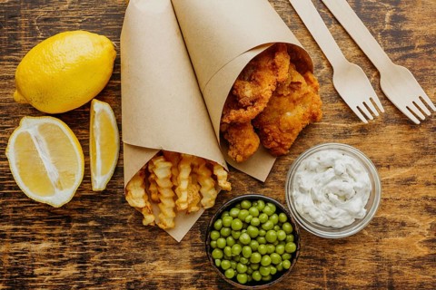 Top view fish chips paper wrap with peas cutlery