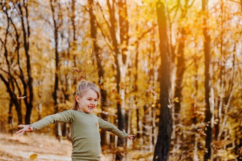 Small happy smiling little caucasian child girl playing with yellow leaves in autumn forest or