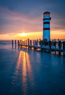 Winter landscape with lighthouse on a lake at sunset