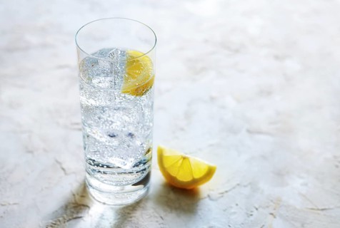 Fresh carbonated mineral water with ice cubes and lemon slices in a drinking glass, refreshing