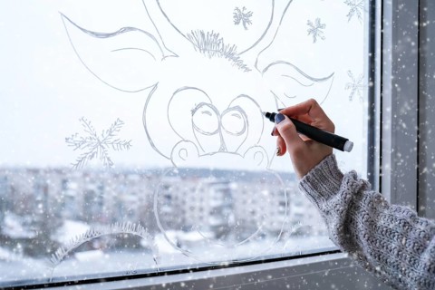 Female hand painting Christmas deer painted on window glass. Christmas winter decor on the window