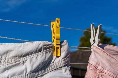 Yellow and white clothes pegs holding pink clothes on a clothesline under a blue sky, Weseke,