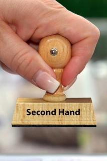 A woman's hand holds a wooden stamp with the inscription: Second Hand
