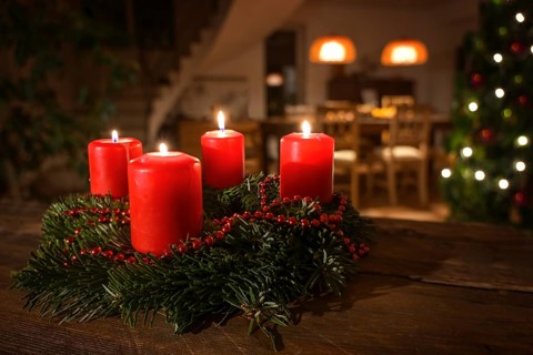 Decorated Advent wreath from fir branches with red burning candles on a dark wooden table, living