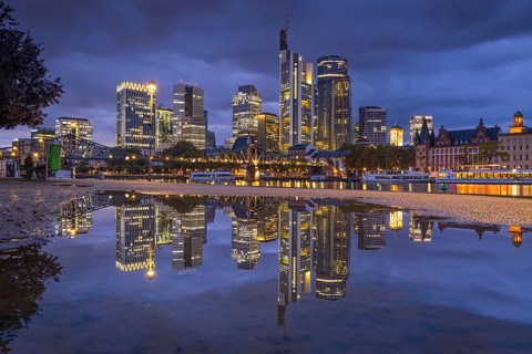 Clouds pass over the glowing Frankfurt bank skyline reflected in a puddle in the evening, Mainufer,
