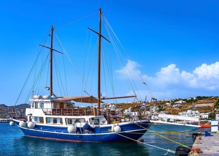 Schooner moored at jetty of typical Greek island. Beautiful whitewashed houses on hills and by
