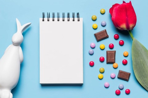 White easter statue spiral notepad tulip gem candies chocolate pieces blue background
