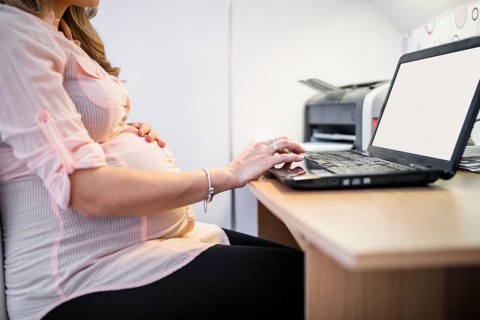 Midsection view pregnant woman using laptop wooden desk