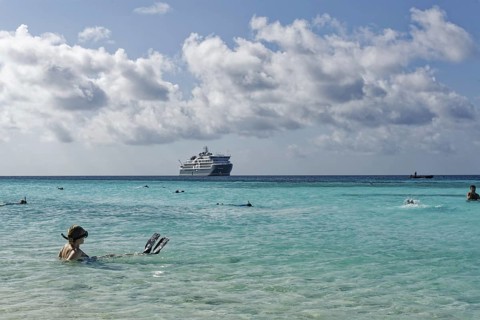 Snorkeller sitting in turquoise blue water, cruise ship SH DIana in the background, blue, slightly