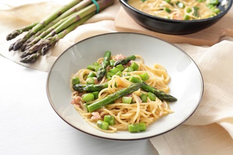 Spaghetti carbonara variation with green asparagus served in a plate, ingredients and napkin on a