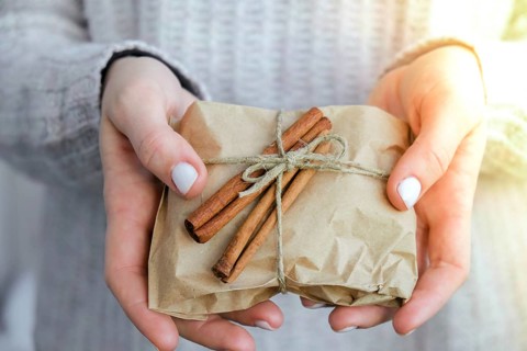 Woman giving Box with New Year's gifts, wrapped in craft paper and decorated with cinnamon sticks.