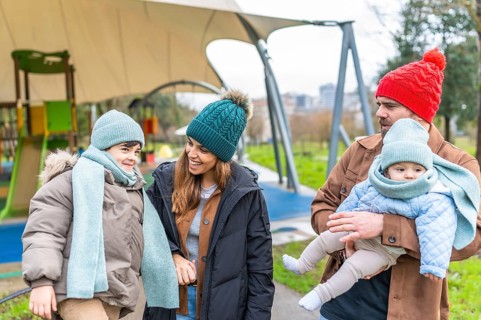 Smiling parents holding their children, a toddler and a baby, wearing warm winter clothes while