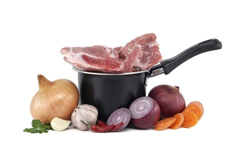 Black saucepan with pieces of raw pork inside. Around the saucepan are sliced vegetables which