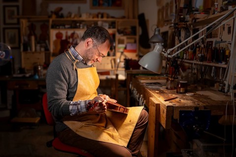 Luthier finishing a violin under controlled lighting, surrounded by woodworking tools in Cremona,