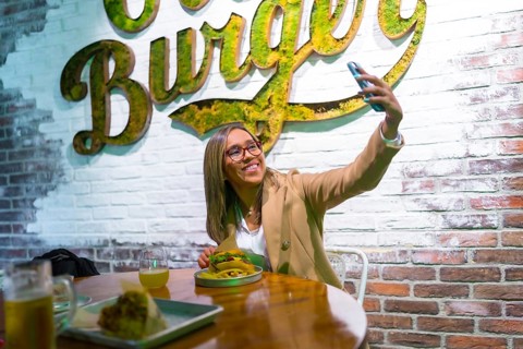 Happy latin blonde woman taking selfie while eating a tasty hamburger at fast food restaurant