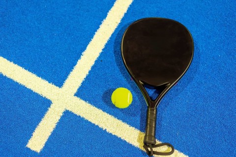 Top view of a single paddle tennis racket and ball in a blue court