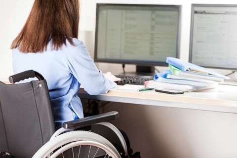Invalid or disabled young business woman person sitting wheelchair working office desk computer