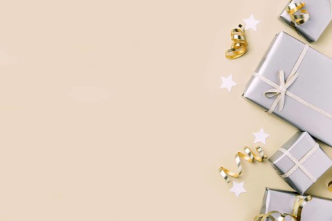 Light beige or yellow flat lay background with gift boxes in glossy silver craft paper packaging
