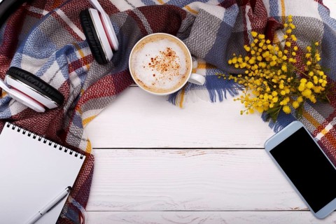 Hot coffee cappucino, blanket, mimosa flowers, notepad, smartphone and head phones on old wooden