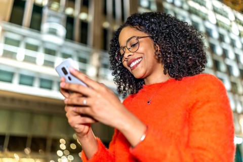 Smiling businesswoman engaging with a mobile phone app while enjoying the vibrant city center at