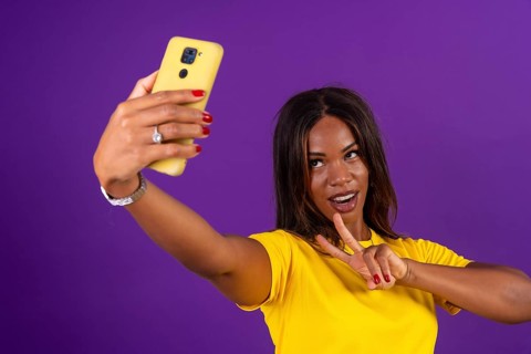 Studio portrait with purple background of an african urban woman gesturing success while taking a