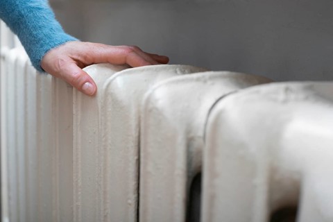 Caucasian female warming up hands near Hot Water Radiator. Space for text