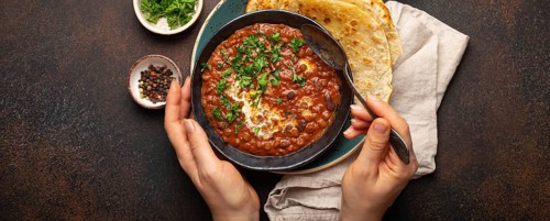 Female hands holding a bowl and eating traditional Indian Punjabi dish Dal makhani with lentils and
