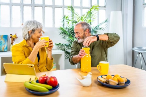 Senior couple enjoying healthy breakfast at home using tablet and talking together