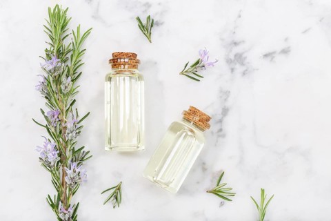 Rosemary essential oil in glass bottle and twigs on marble table. Salvia Rosmarinus oil. Top view