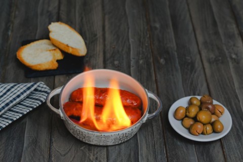 Typical spanish tapa, chorizo al infierno in ceramic casserole accompanied by bread and olives