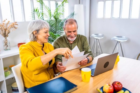 Senior couple working together on their home budget using laptop and holding papers