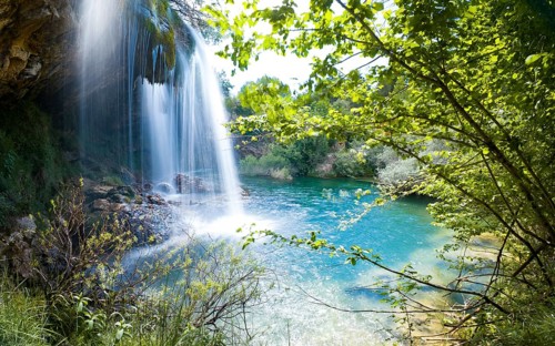 A serene waterfall surrounded by lush greenery pouring into a turquoise pool of water