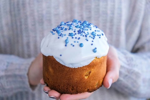 The cook Hands hold Easter cake with white topping and blue sprinkles. Woman holding traditional