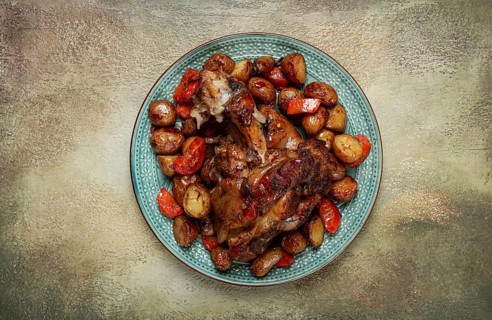 Pork knuckle baked with vegetables, new potatoes, on a plate, homemade, no people