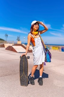 Asian woman holding a skateboard and adjusting her cap standing on a skateboard park
