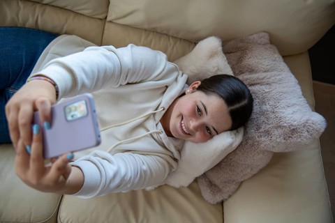 Overhead view of a young Caucasian woman lying on a sofa, capturing a selfie. Moment of joy and